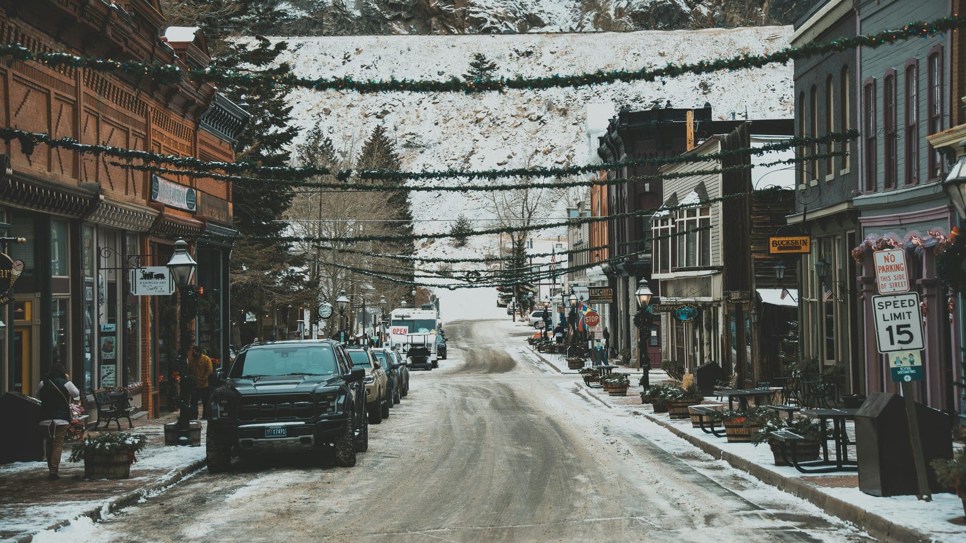 Snow-covered main street in a ski town at dusk with lit storefronts